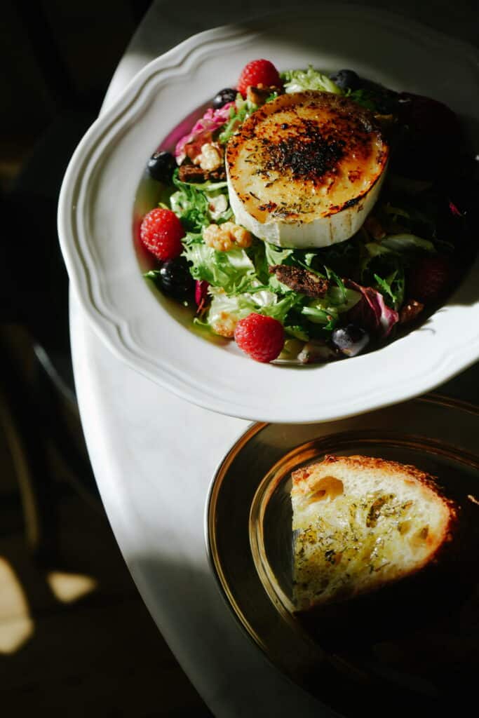 Grillet gedeost med friske bær og salat på elegant tallerken.